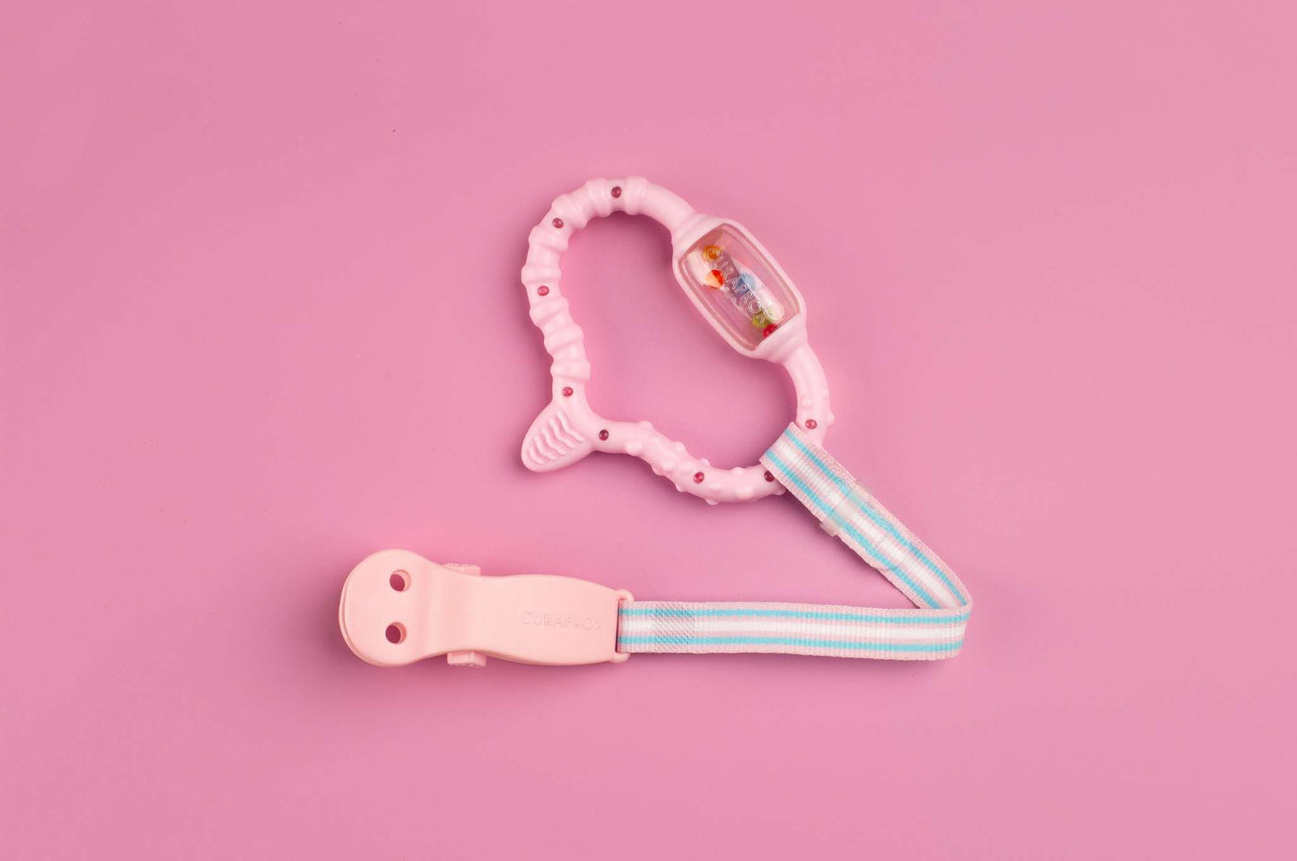 Curaprox Baby pink teething ring with textured design and striped strap on pink background
