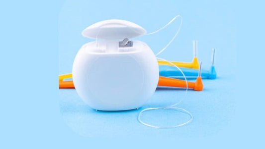 white dental floss container with floss thread and colorful interdental brushes on blue background