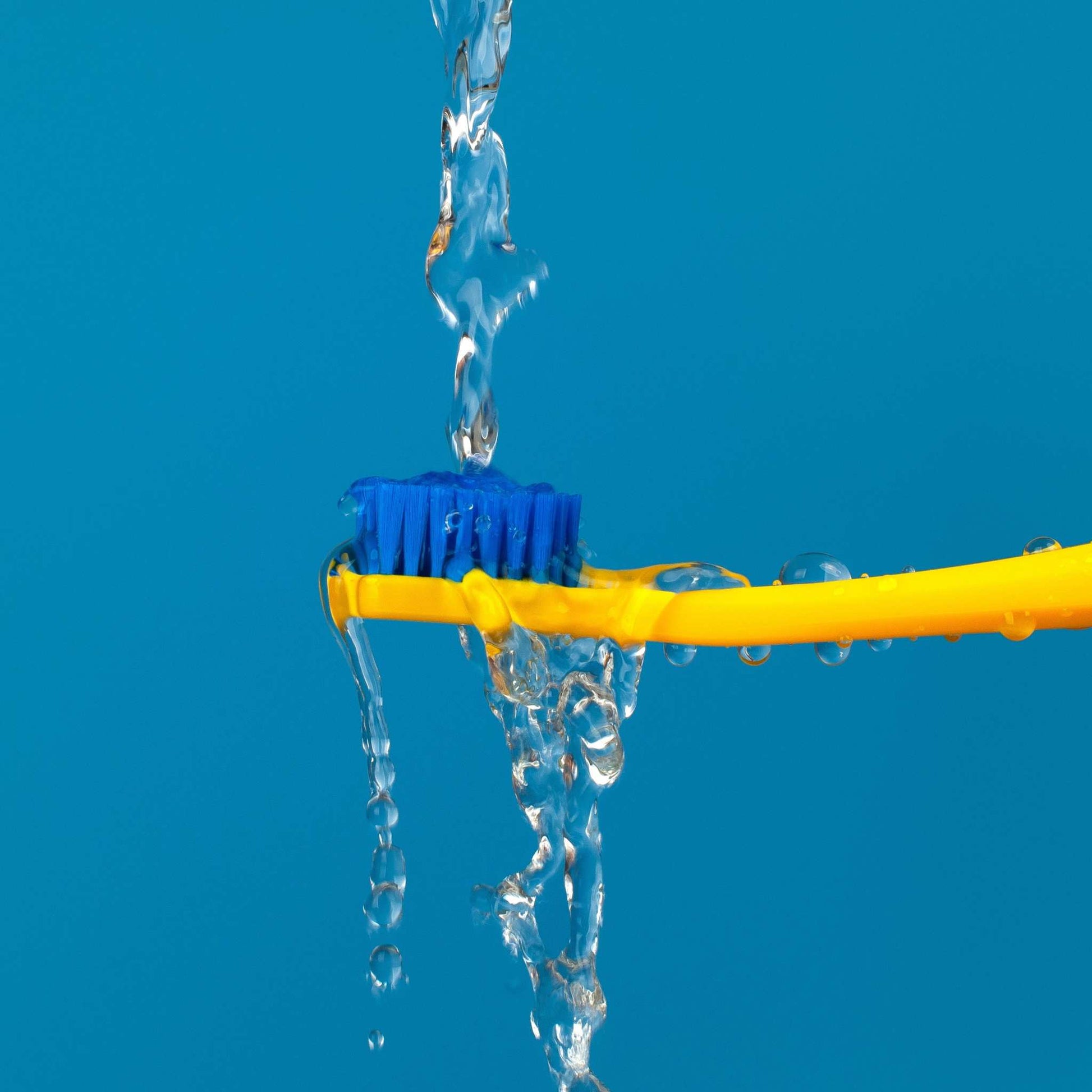 Curaprox CS 5460 ultra soft toothbrush with blue bristles and yellow handle under running water against blue background