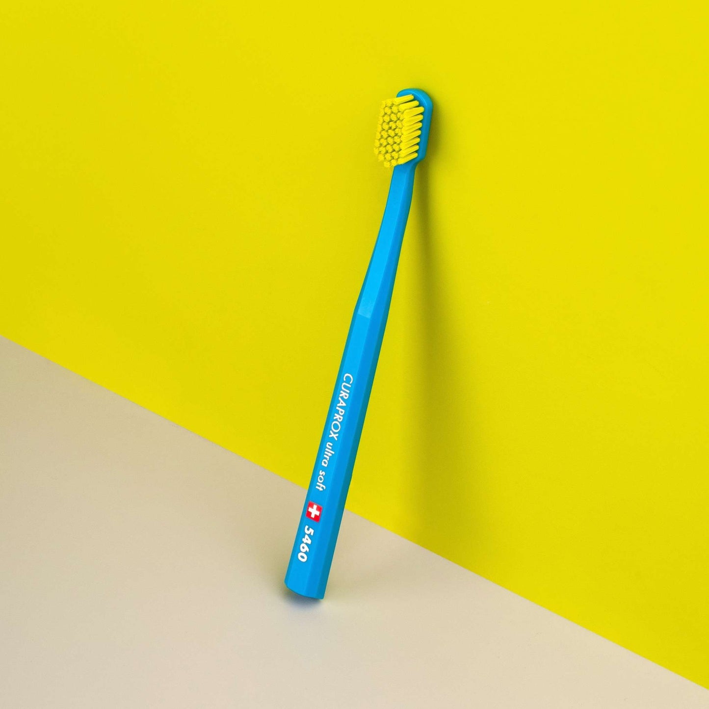Curaprox CS 5460 ultra soft toothbrush with dense yellow bristles and blue handle against yellow background