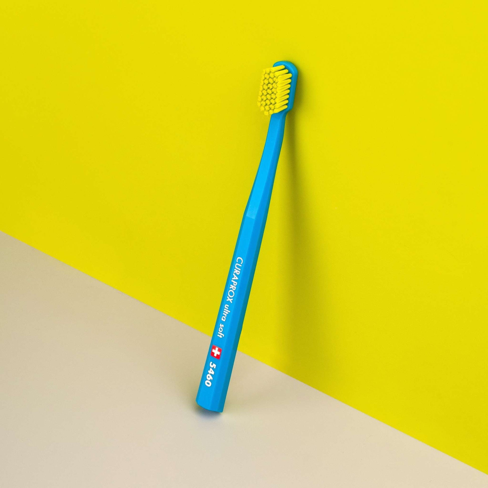 Curaprox CS 5460 ultra soft toothbrush with dense yellow bristles and blue handle against yellow background