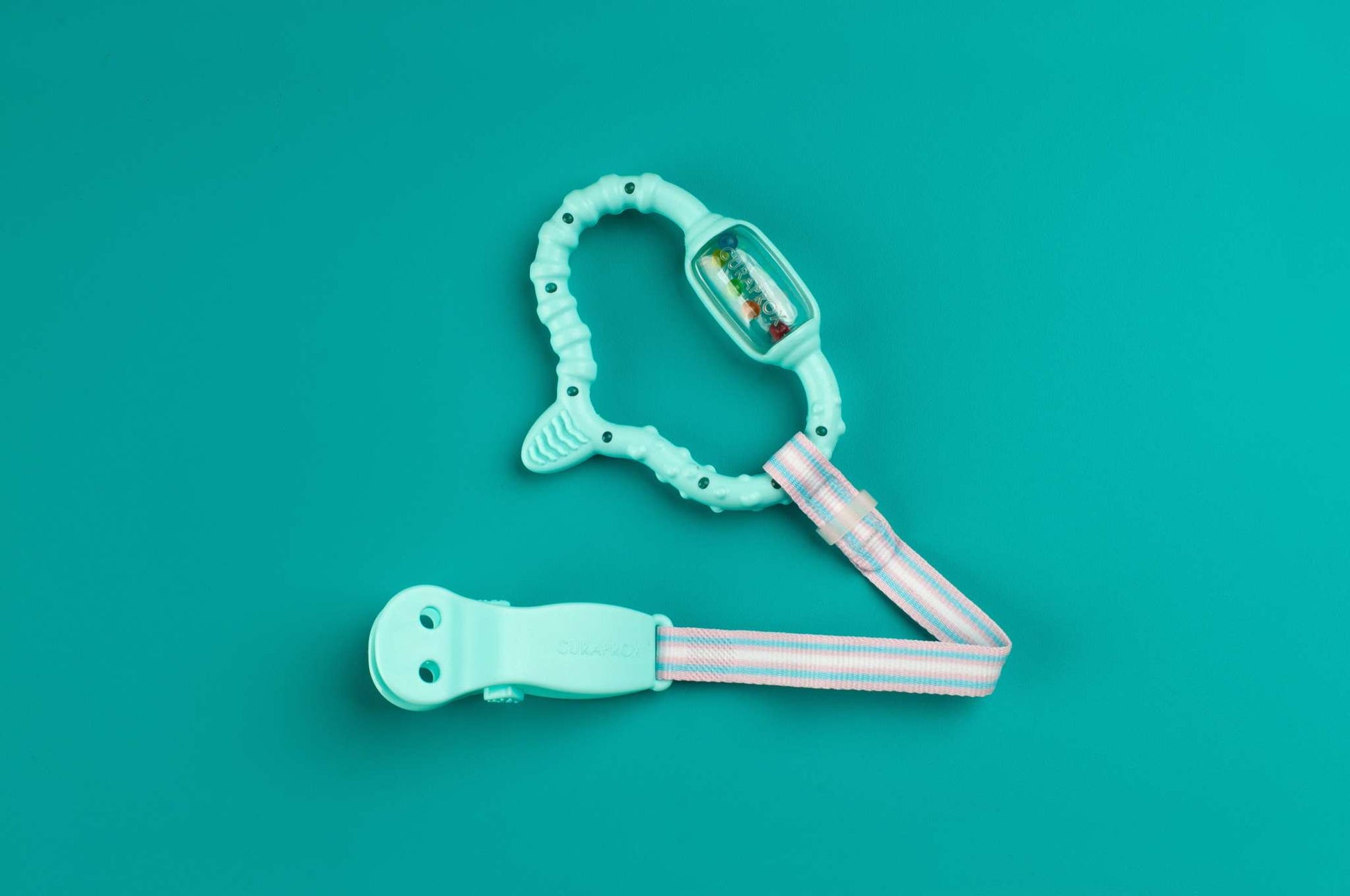 Curaprox Baby turquoise teething ring with strap against teal background