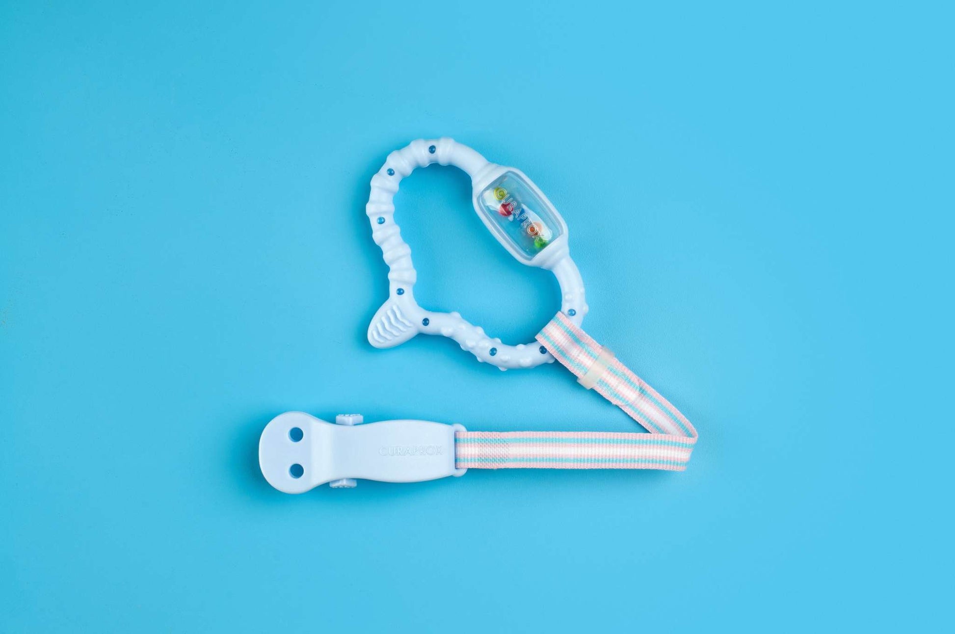 Curaprox Baby teething ring with clip and bead rattle on blue background