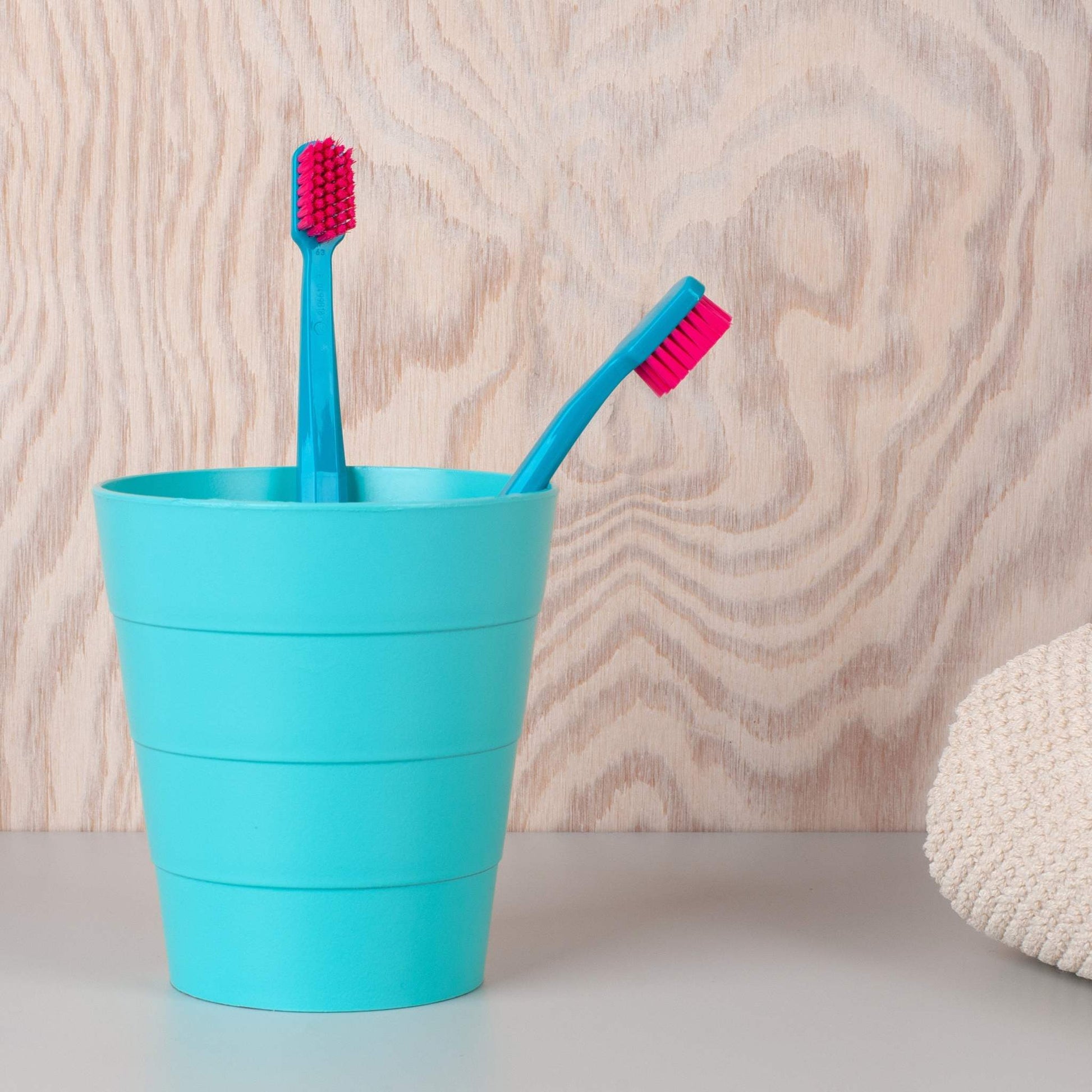 Two Curaprox CS 5460 ultra soft toothbrushes with pink bristles in a turquoise cup against a wooden background