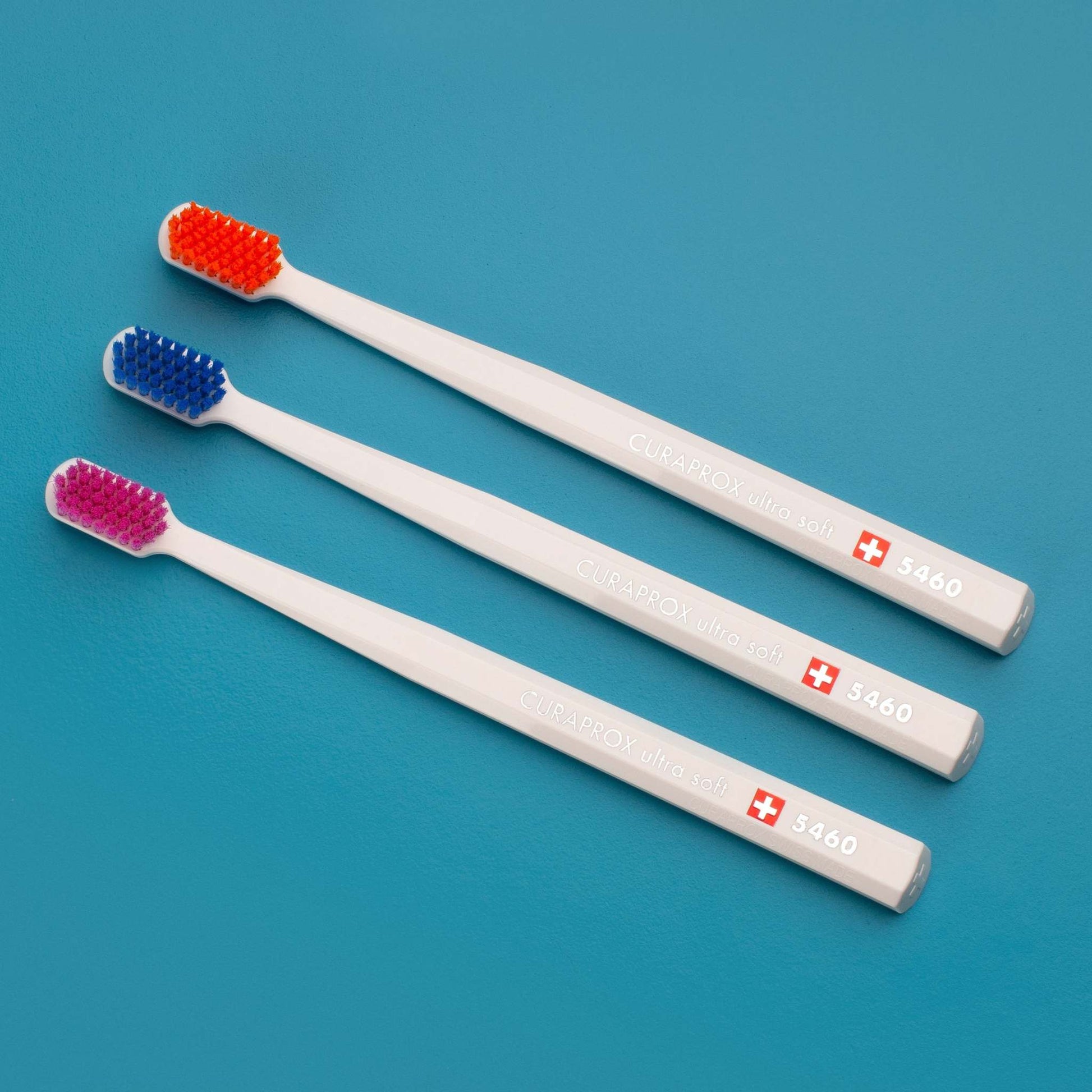 Curaprox CS 5460 ultra soft toothbrushes with assorted colored bristles and ergonomic white handles on blue background