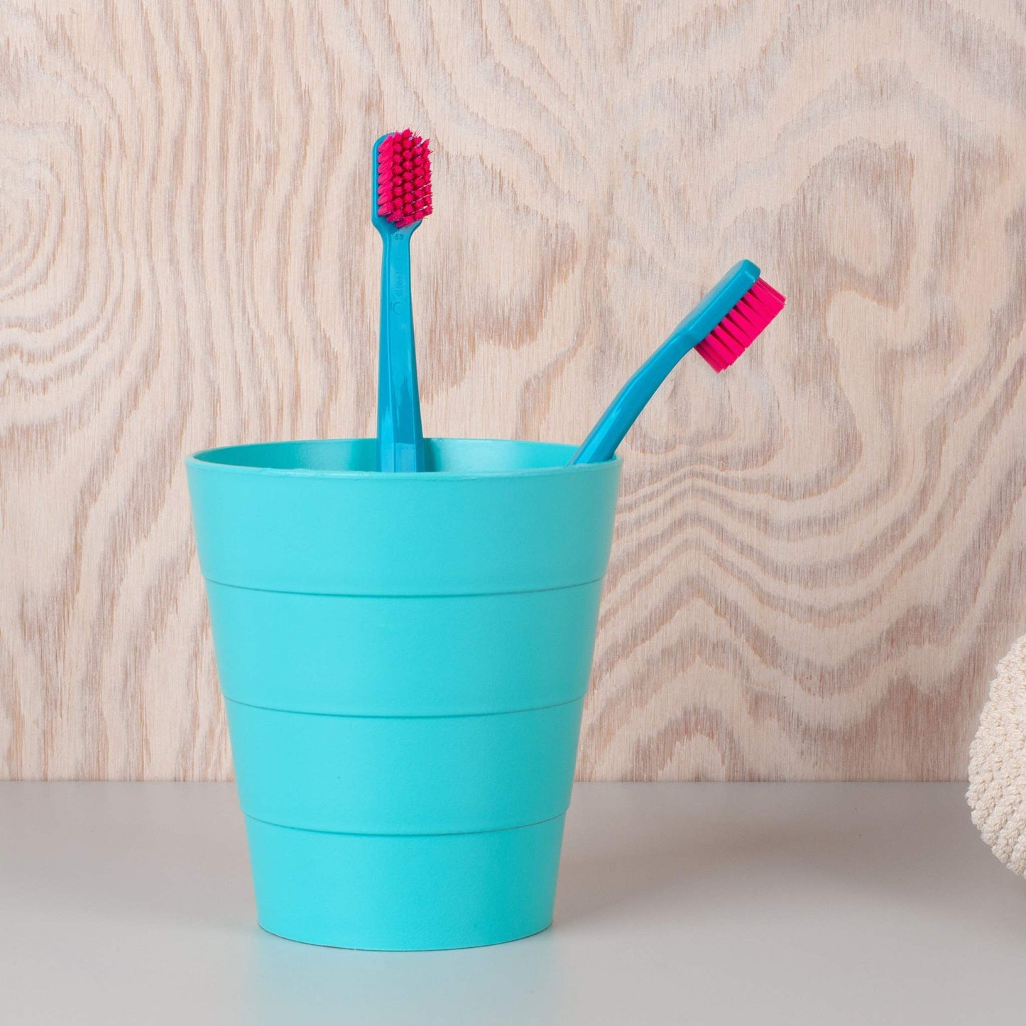 Two Curaprox CS 5460 ultra soft toothbrushes with pink bristles in a turquoise holder against a wooden background