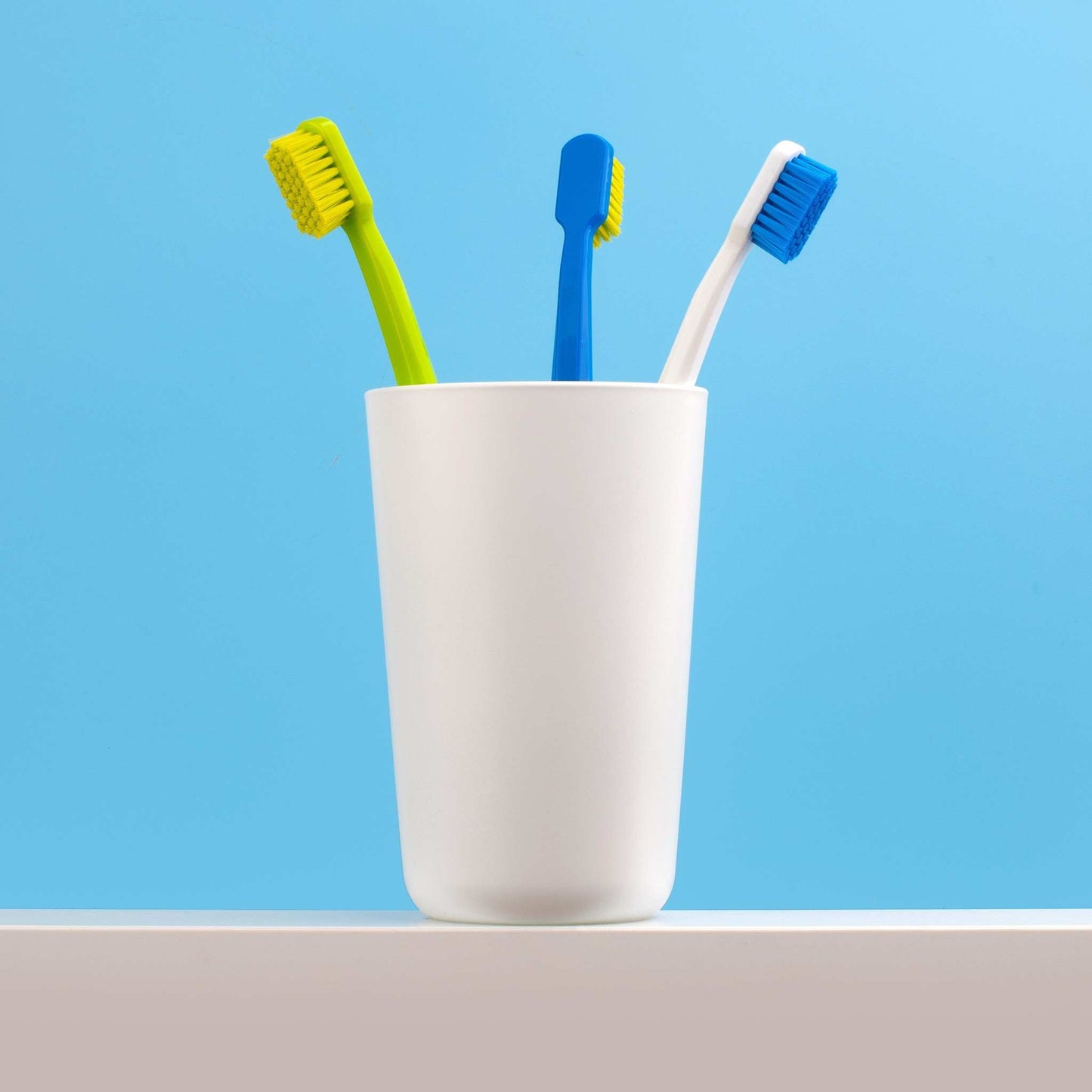 Three assorted coloured Curaprox CS 5460 ultra soft toothbrushes in a white holder against a blue background