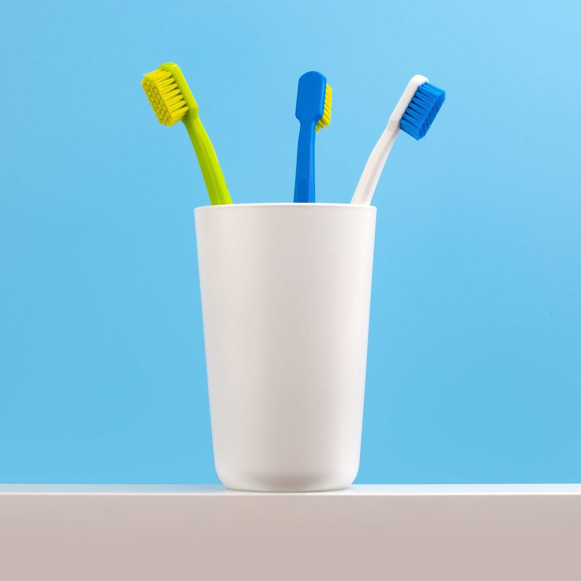 Three assorted coloured Curaprox CS 5460 ultra soft toothbrushes in a white holder against a blue background