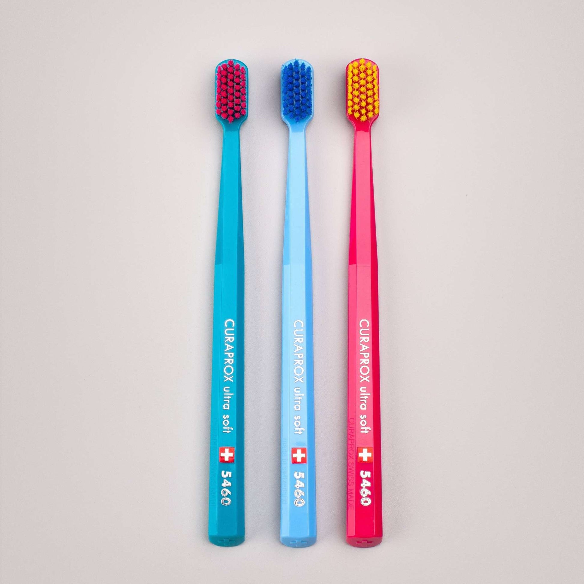 Three Curaprox CS 5460 ultra soft toothbrushes in blue, light blue, and pink with densely packed bristles.