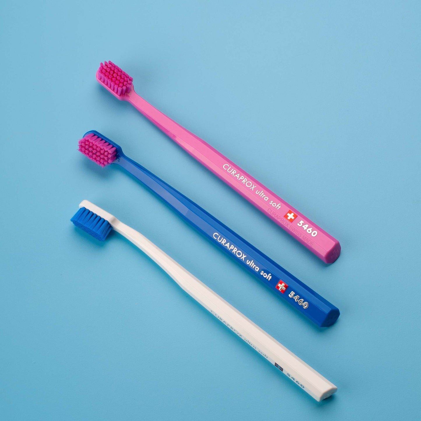Curaprox CS 5460 ultra-soft toothbrushes in pink, blue, and white with dense fine bristles and ergonomic handles for gentle effective cleaning
