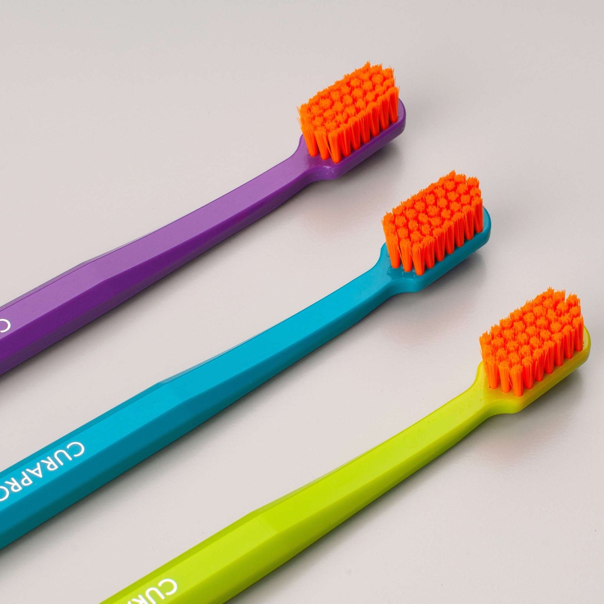 Curaprox CS 5460 ultra soft toothbrushes in purple, blue, and green with orange bristles for gentle and effective cleaning.