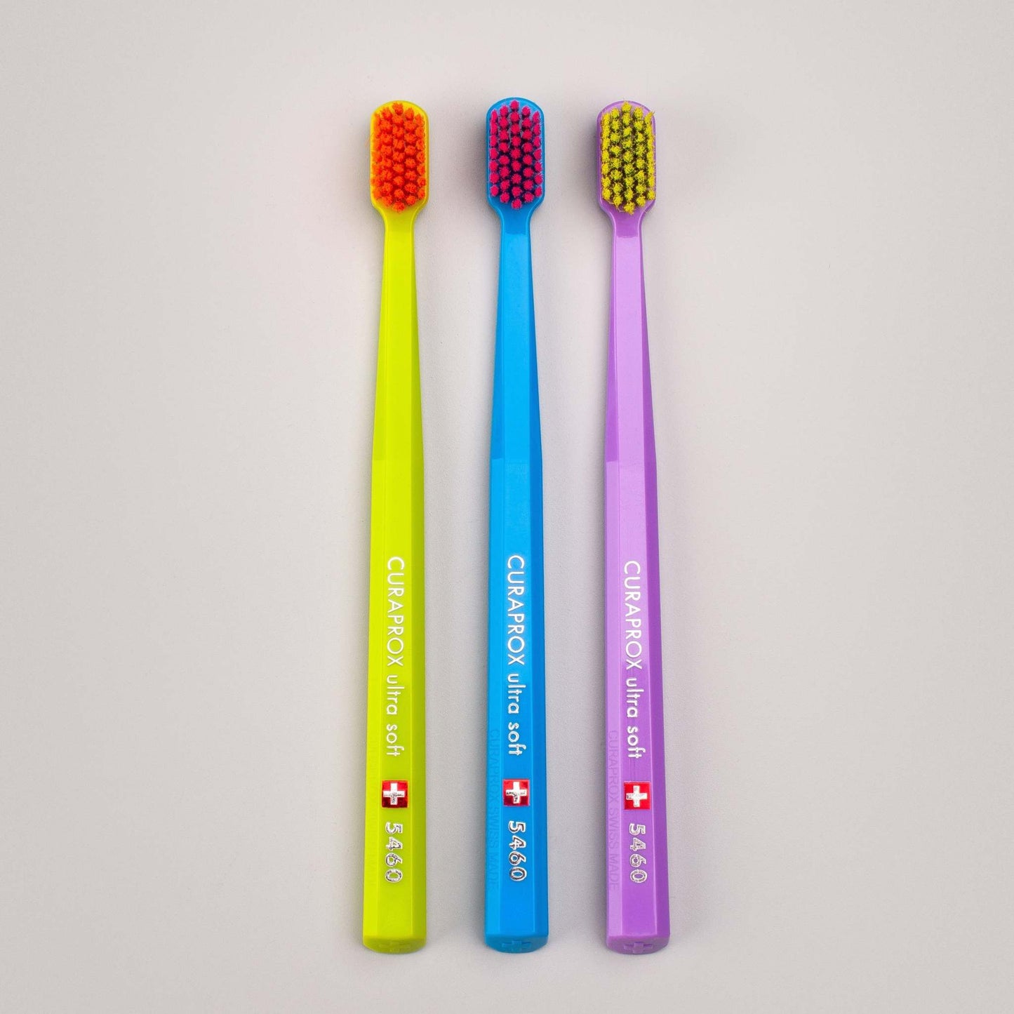 Three Curaprox CS 5460 ultra soft toothbrushes in yellow, blue, and purple with densely packed bristles for gentle and effective cleaning