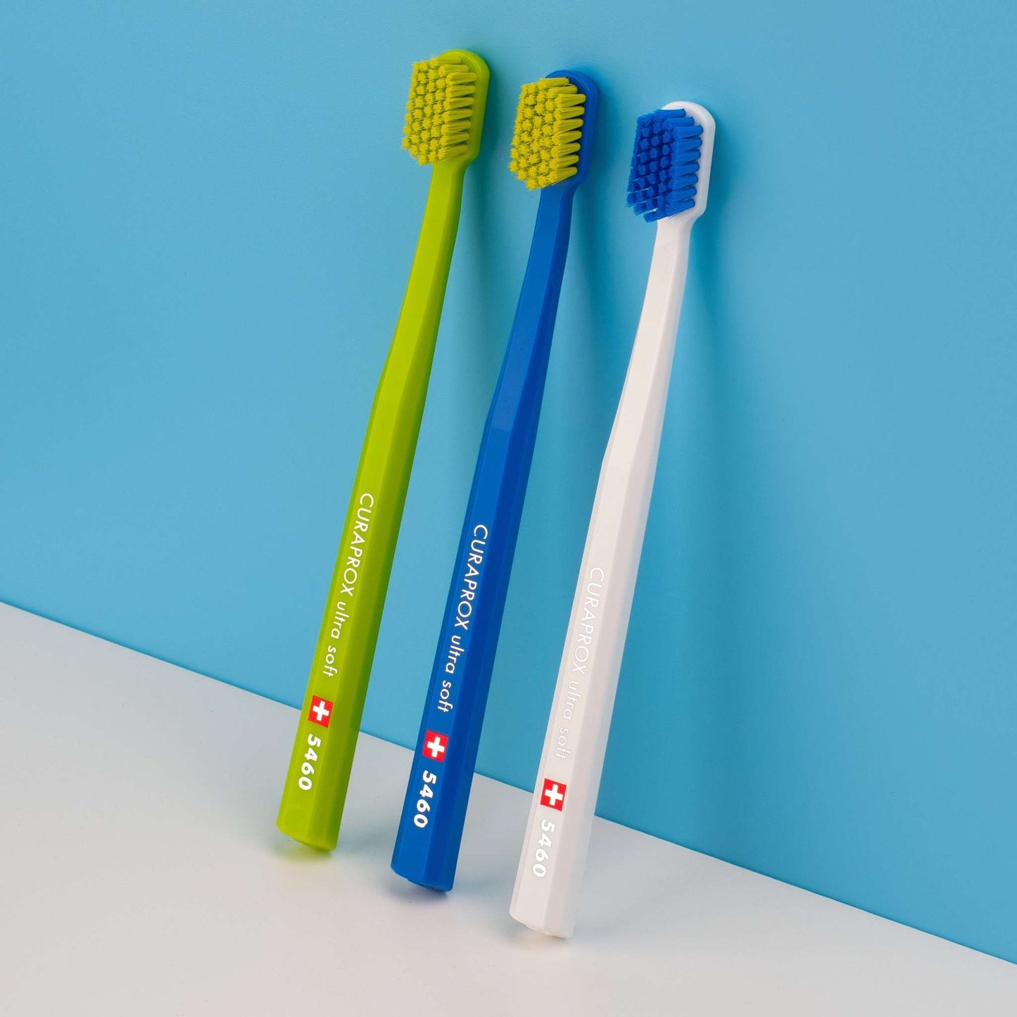 Three Curaprox CS 5460 ultra soft toothbrushes in green, blue, and white with dense bristles for gentle, effective dental care