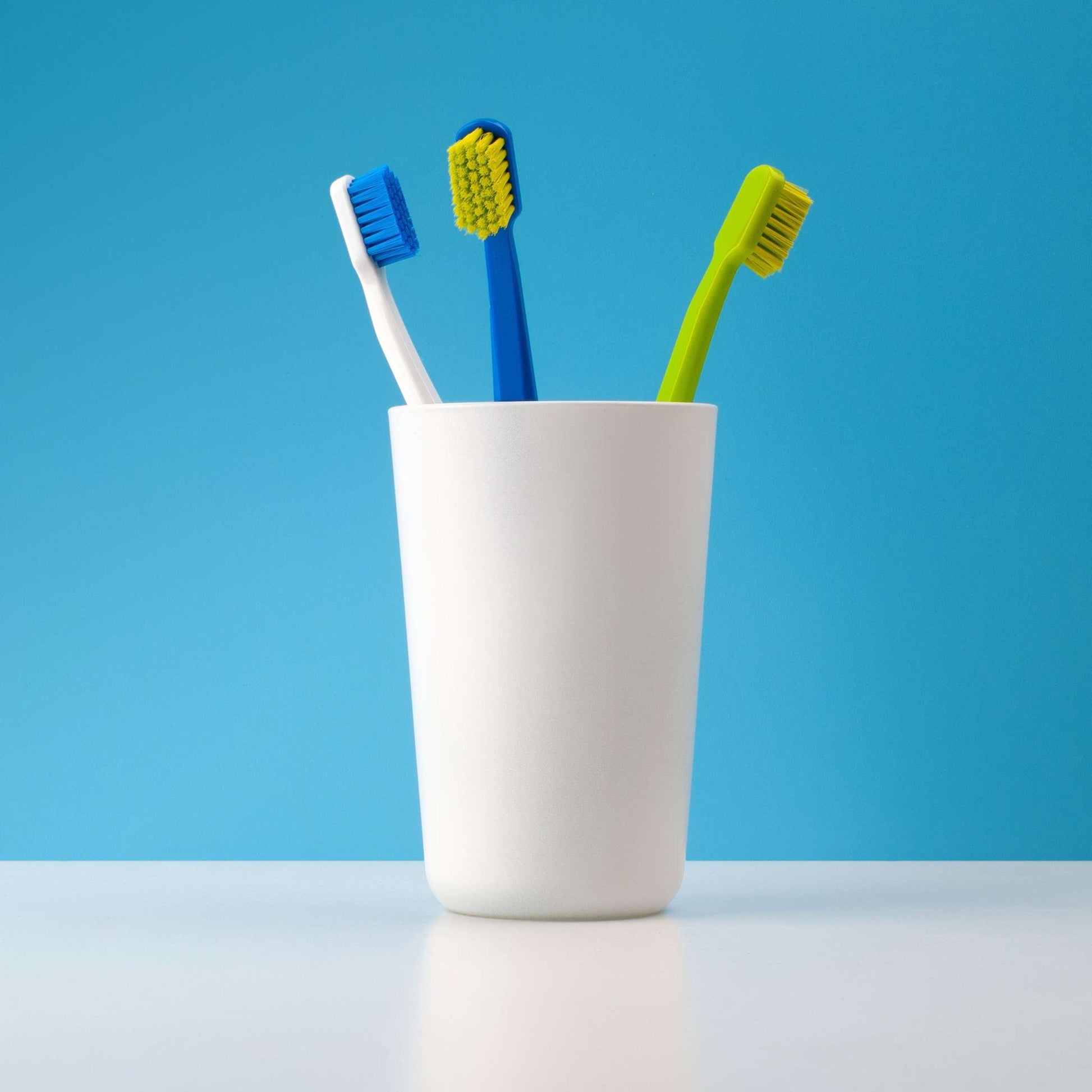 Three Curaprox CS 5460 ultra soft toothbrushes with assorted colors in a white cup against blue background