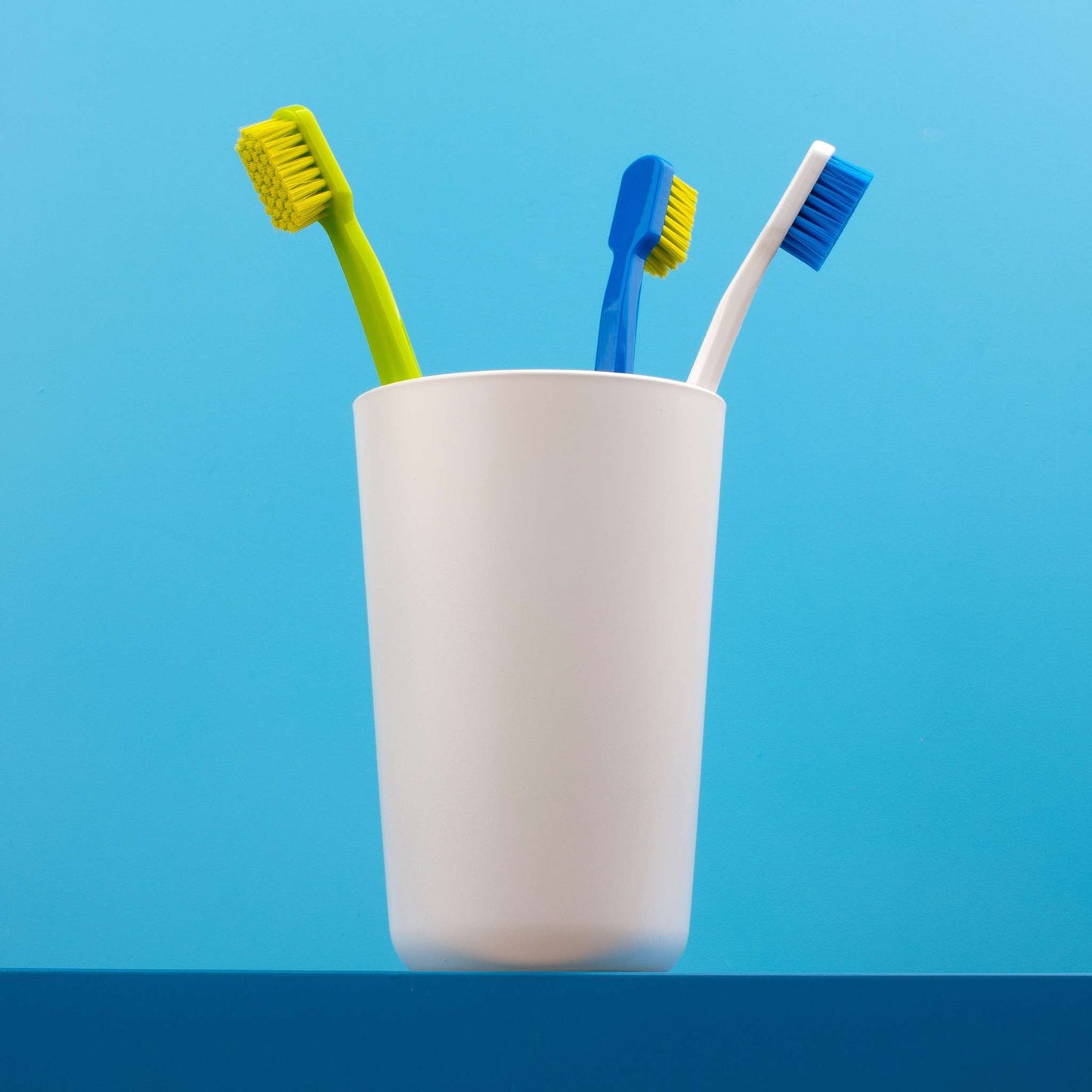 Assorted Curaprox CS 5460 ultra soft toothbrushes with densely packed bristles in a white cup against blue background