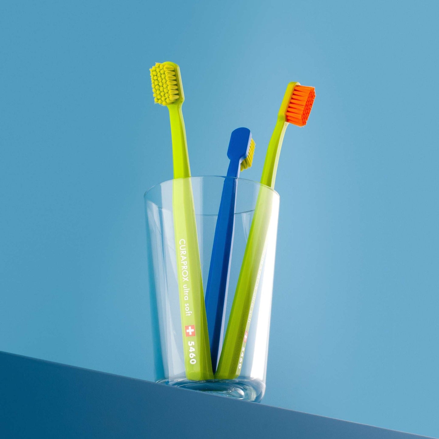 Curaprox CS 5460 ultra soft toothbrushes with dense bristles in assorted colors in a clear glass on blue background