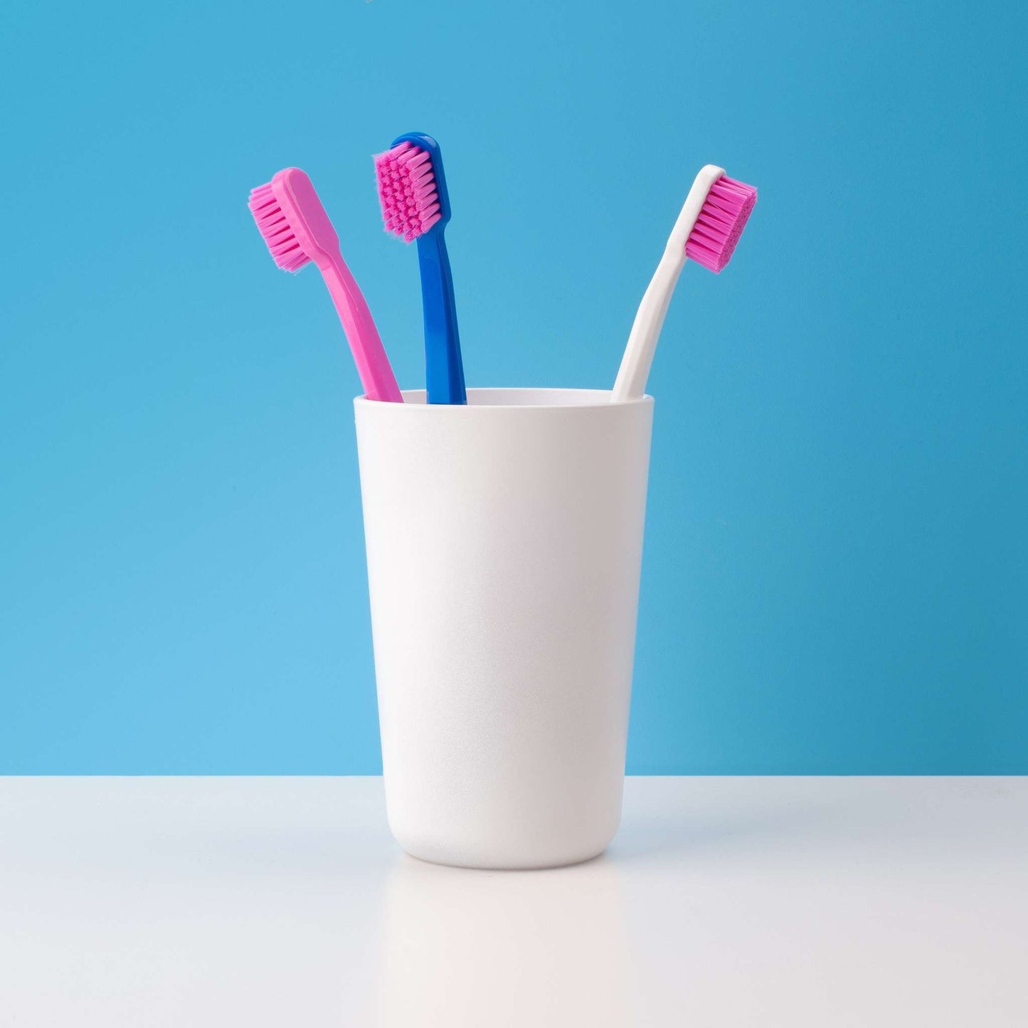 Curaprox CS 5460 ultra soft toothbrushes in assorted colors standing in a white cup against a blue background