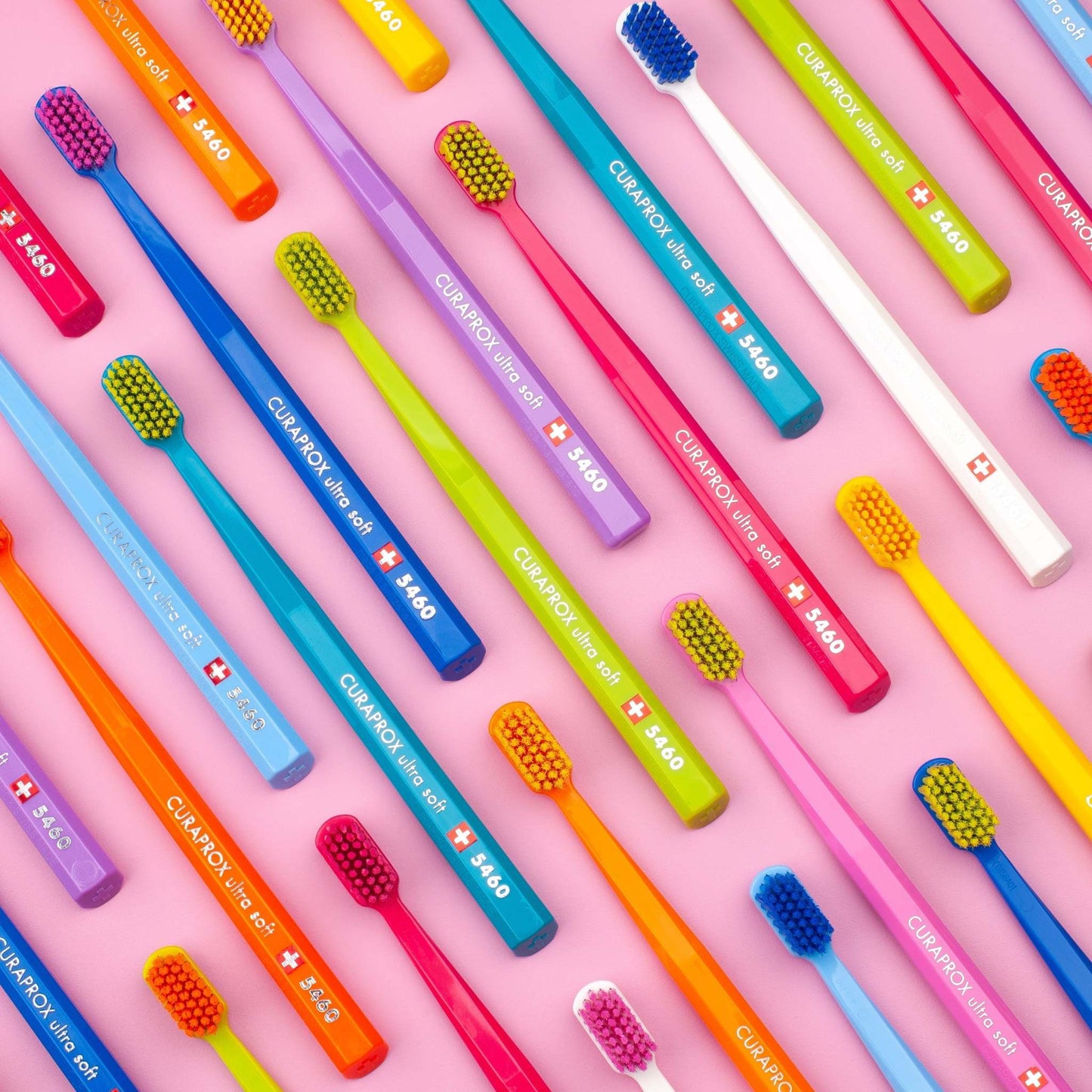 Multiple colorful Curaprox CS 5460 ultra soft toothbrushes arranged on a pink background