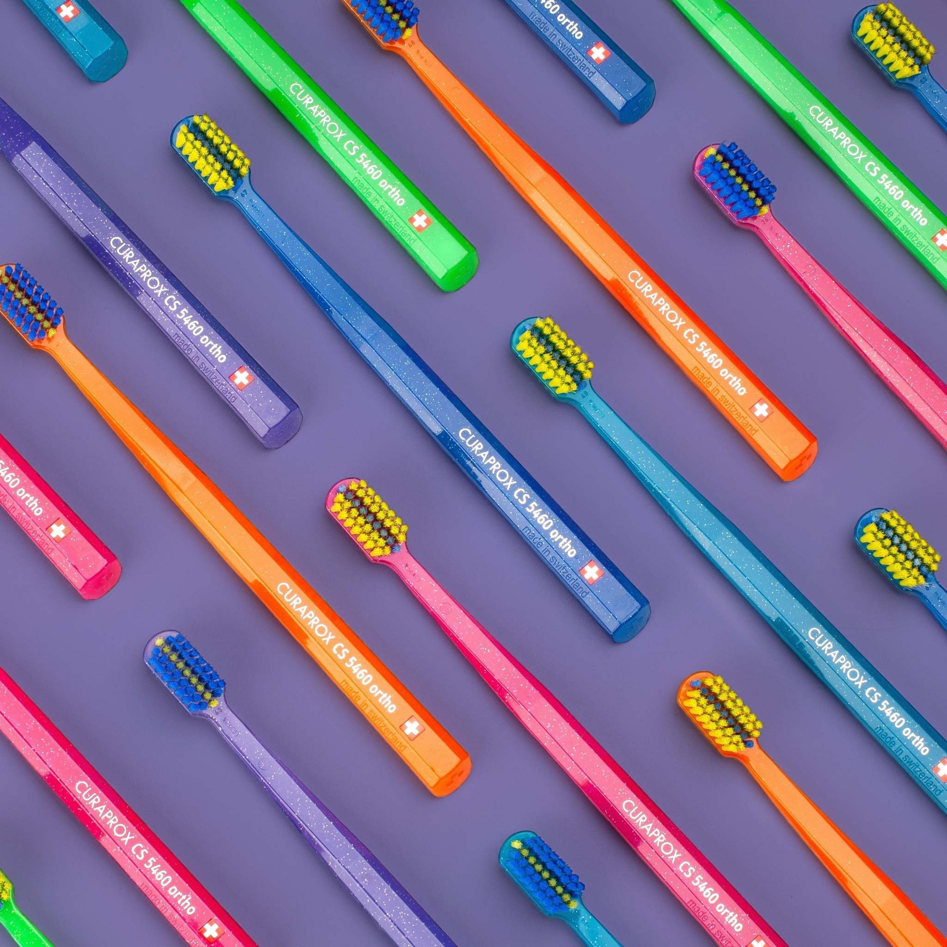 Curaprox CS 5460 orthodontic toothbrushes in multiple colors with ultra-soft bristles on purple background