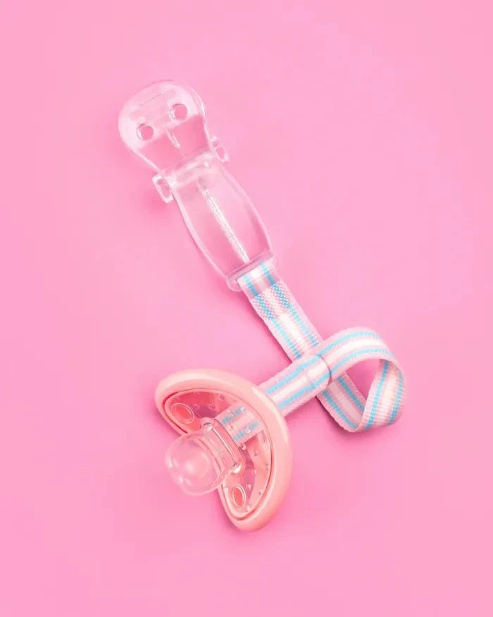 Clear Curaprox Baby Soother Holder with pastel striped strap attached to a pink pacifier on pink background